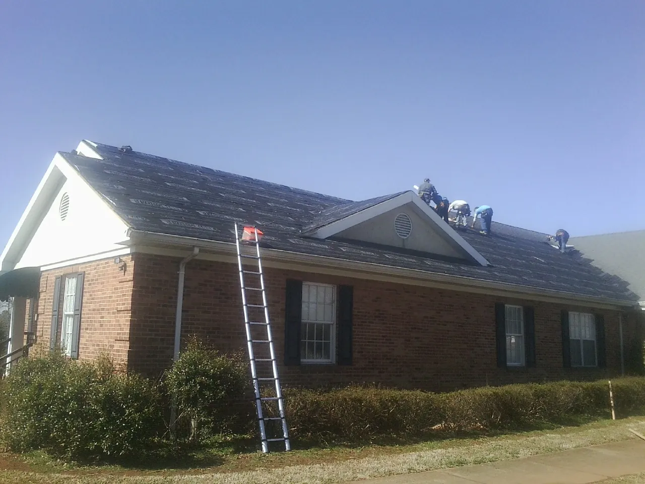 Crew tearing shingles off a brick ranch roof with a ladder set — Emergency Roof Repair work by our crew in Olin