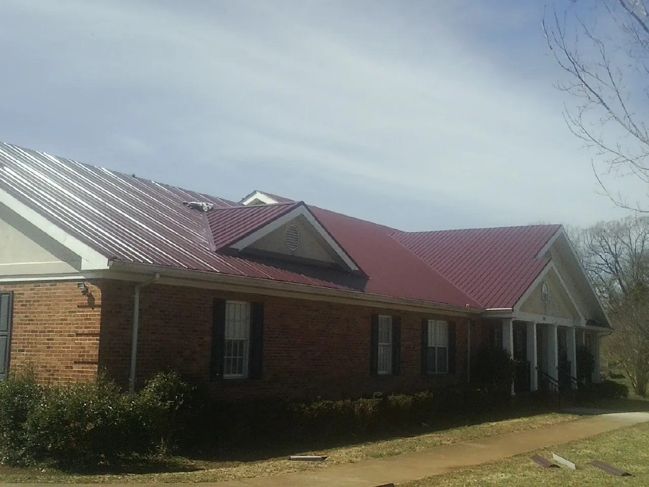 Red metal roof with gabled entries on a long brick building, from a Hail Damage Roof Repair job in Olin